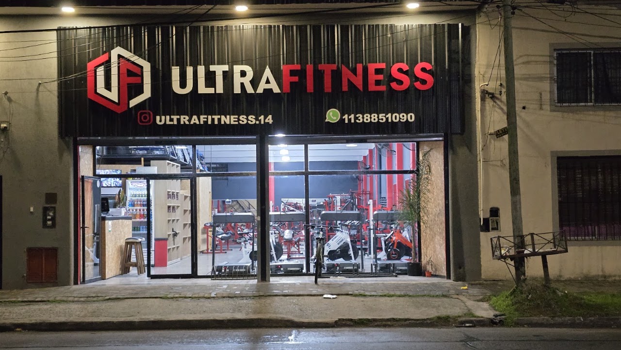 Fachada exterior de Ultrafitness Berazategui Oeste iluminada de noche con ventanales y luces rojas